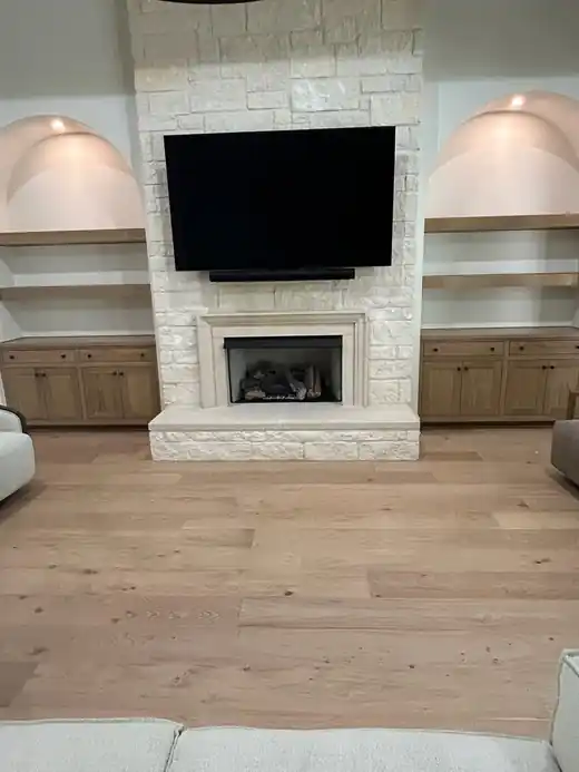 A finished gas fireplace set in a white stone wall below a mounted TV