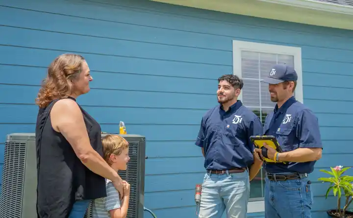 Two TDi technicians talking with a homeowner and her son beside the condenser