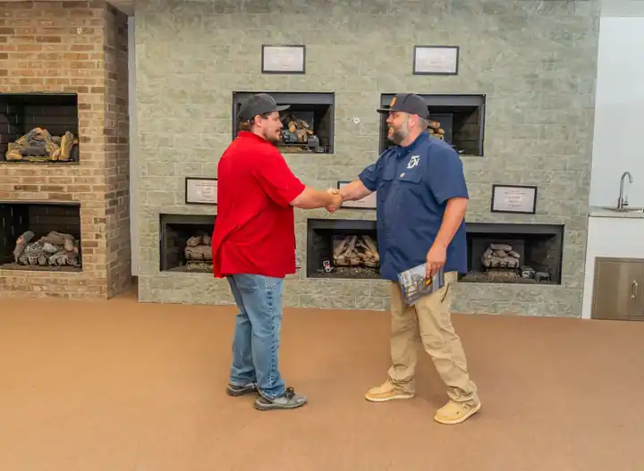A TDi staff member shaking a customer's hand in front of the fireplace wall of gas logs in the showroom